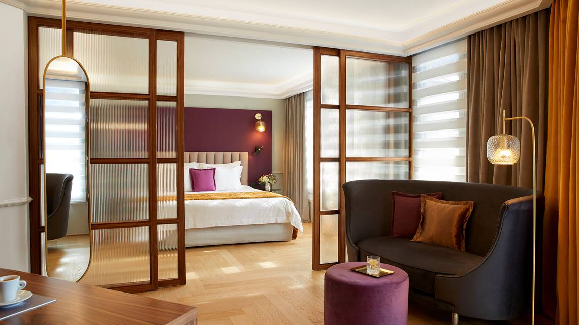 Penthouse Suite with modern sitting area, glass sliding doors and bedroom view at The Excelsior Hotel