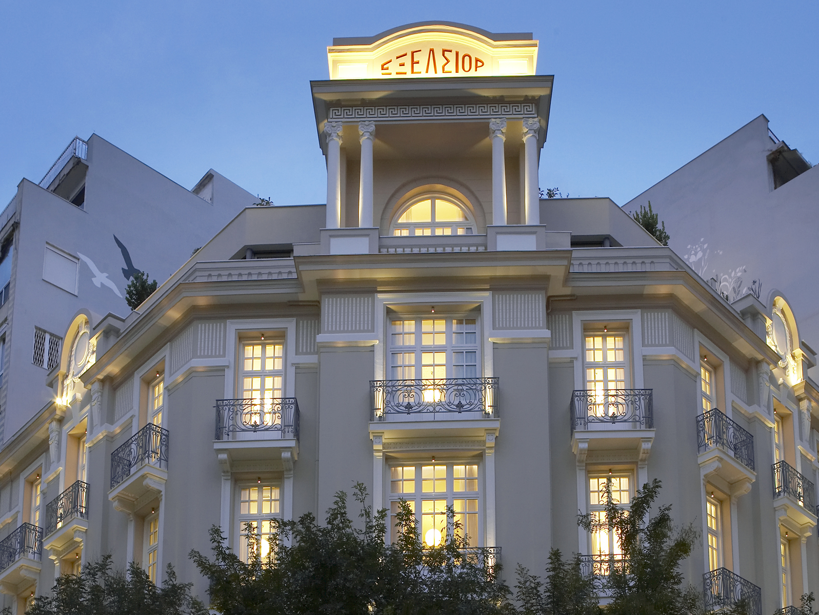 
Illuminated facade of The Excelsior Hotel with balconies and neoclassical architecture at dusk