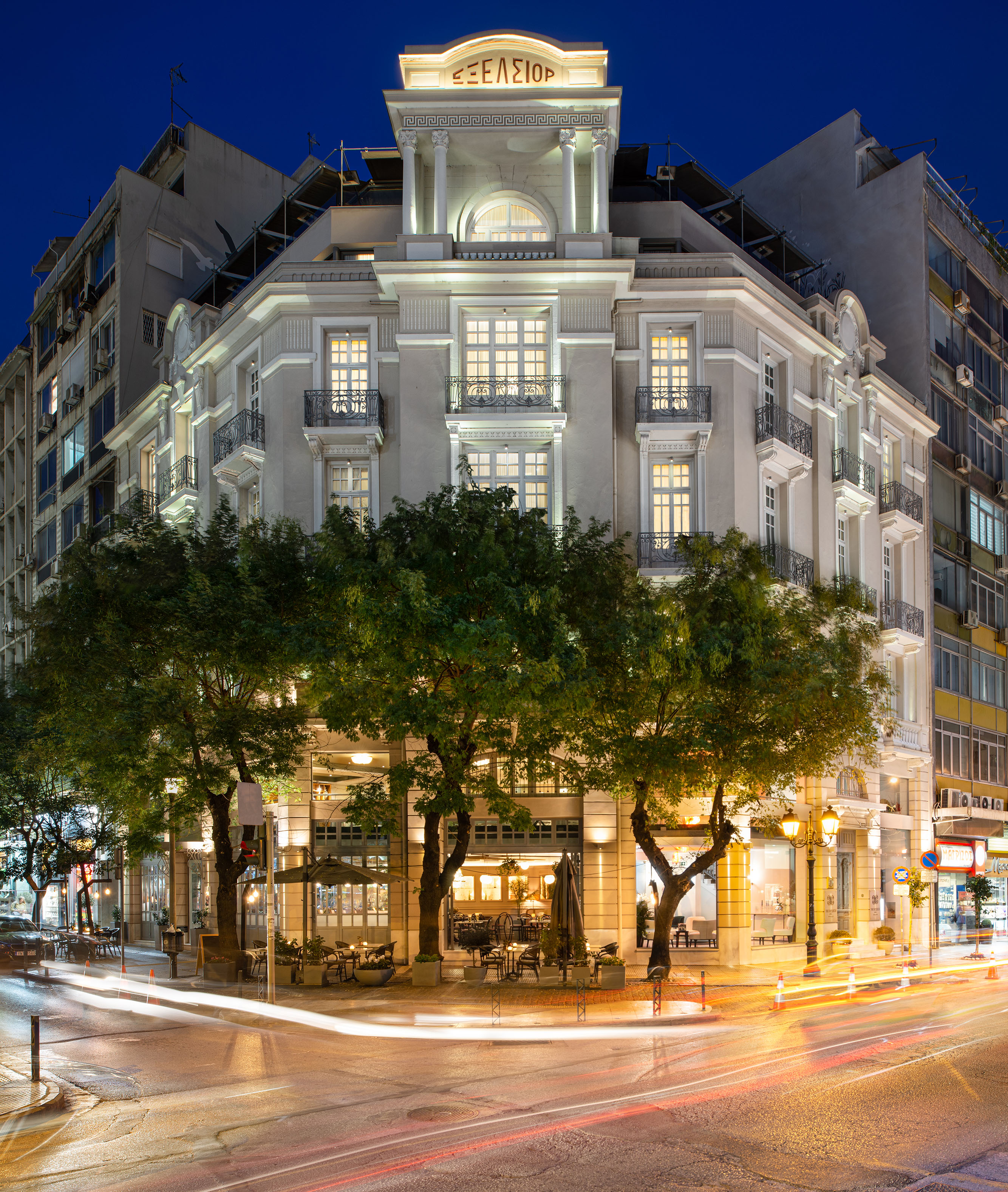 
The Excelsior Hotel illuminated at night with neoclassical facade, balconies and street cafe